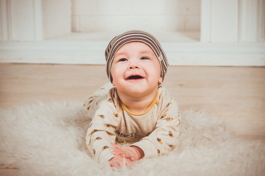 A happy, smiling baby laying on their tummy on a white fluffy rug.
