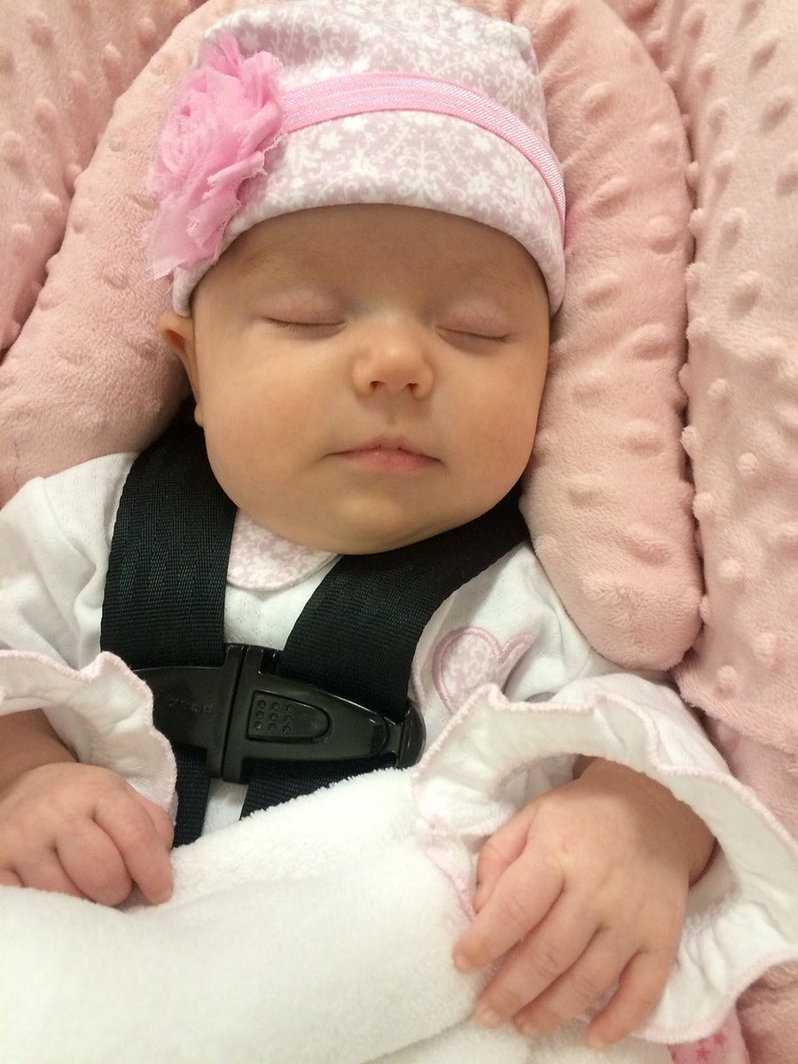 A blissfully sleeping baby comfortable and secure in a plush pink safety car seat.